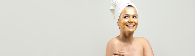 Retrato da beleza da mulher na toalha branca na cabeça com máscara nutritiva de ouro no rosto Skincare limpeza eco spa cosmético orgânico relax conceito