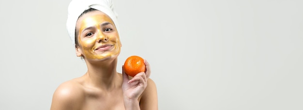 Retrato da beleza da mulher na toalha branca na cabeça com máscara nutritiva de ouro no rosto