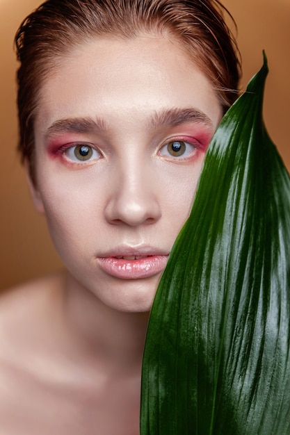 Retrato da beleza de jovem morena com maquiagem de moda de pele perfeita e folha verde sobre fundo marrom natural. Limpeza cosmética orgânica eco conceito de relaxamento e cuidados com a pele. Spa e bem-estar.