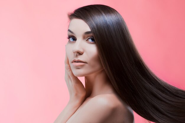 Retrato da beleza de morena com cabelo perfeito, em uma parede rosa. Cuidado capilar