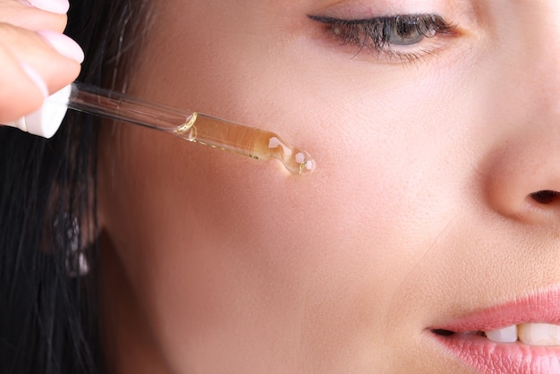 Retrato da beleza de uma garota segurando um conta-gotas com óleo cosmético ou soro perto de rosto limpo