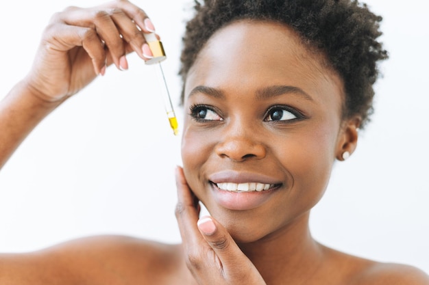 Retrato da beleza de uma jovem africana sorridente em cueca com óleo cosmético para o rosto