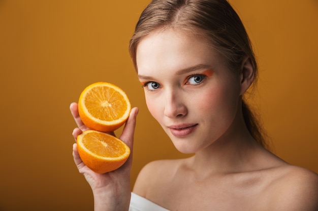 Retrato da beleza de uma jovem loira usando maquiagem isolada, mostrando as duas metades de uma fruta laranja