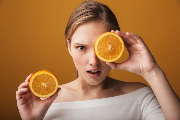 Retrato da beleza de uma jovem loira usando maquiagem isolada, mostrando as duas metades de uma fruta laranja