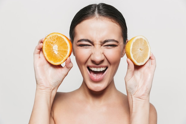 Retrato da beleza de uma jovem morena atraente e saudável, de pé isolado, posando com fatias de limão e laranja