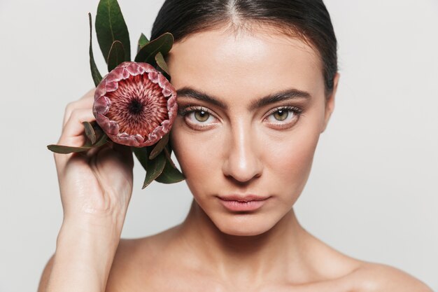 Retrato da beleza de uma jovem morena atraente e saudável, isolada, segurando uma flor no rosto