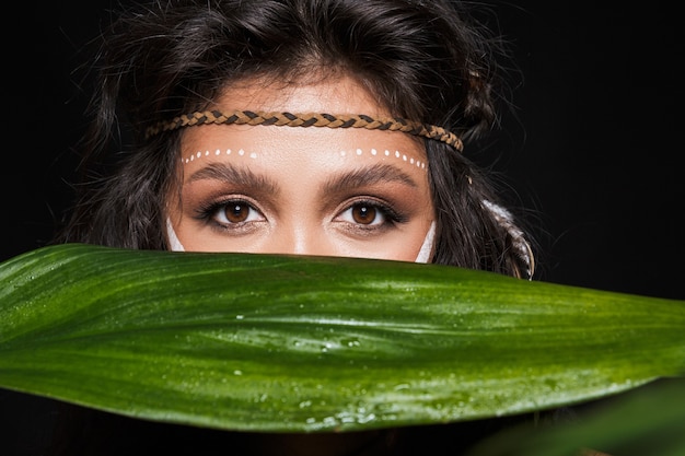 Foto retrato da beleza de uma jovem morena atraente usando acessórios tribais posando com folhas tropicais isoladas.