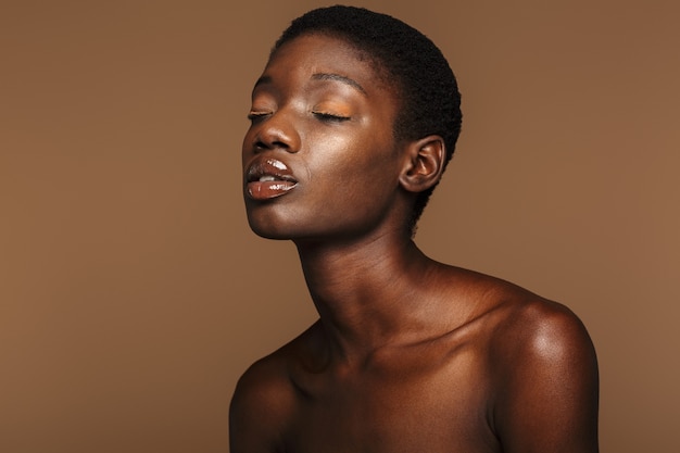 Retrato da beleza de uma jovem mulher africana seminua com cabelo preto curto isolado em bege.