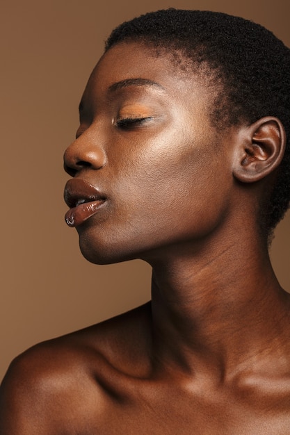 Foto retrato da beleza de uma jovem mulher africana seminua com cabelo preto curto isolado em bege.