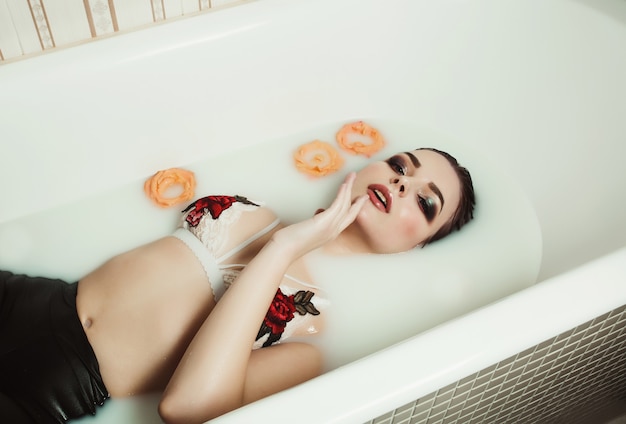 Retrato da beleza de uma linda garota loira tomando banho de leite e rosas