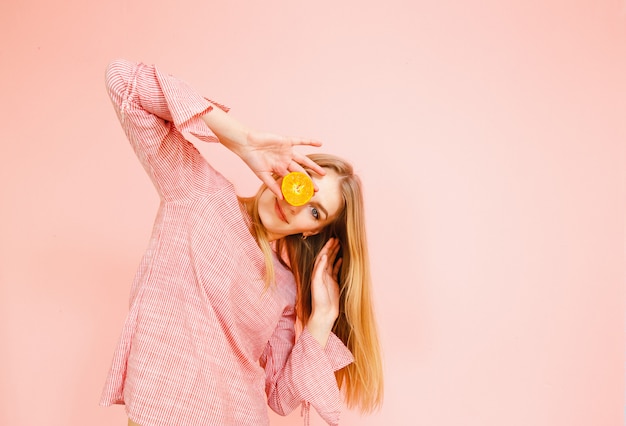 Retrato da beleza de uma mulher atraente saudável posando com um mandarim amarelo isolado sobre fundo rosa.