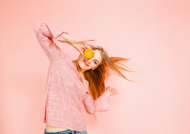 Retrato da beleza de uma mulher atraente saudável posando com um mandarim amarelo isolado sobre fundo rosa.