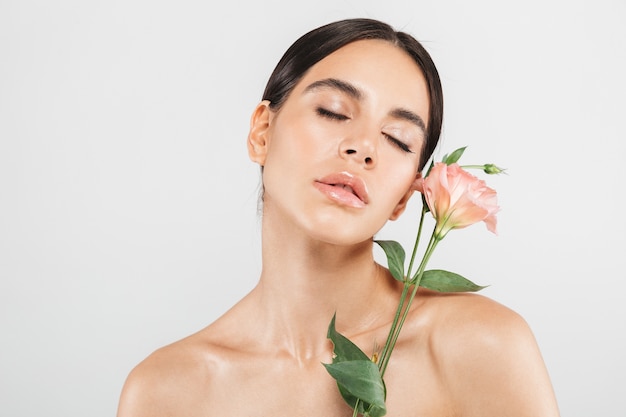 Retrato da beleza de uma mulher atraente sensual e saudável em pé isolado sobre uma parede branca, posando com uma flor