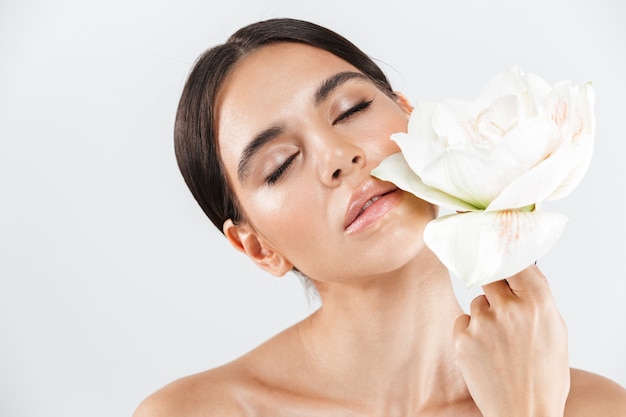 Retrato da beleza de uma mulher atraente sensual e saudável em pé isolado sobre uma parede branca, posando com uma flor