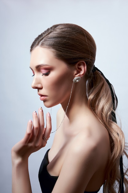 Retrato da beleza de uma mulher com cabelo comprido, brincos nas orelhas e joias caras nas mãos