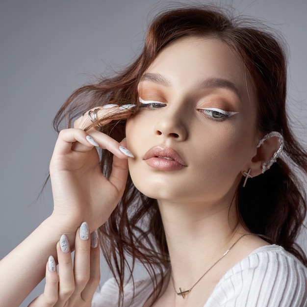 Retrato da beleza de uma mulher com maquiagem natural e unhas pintadas na mão.