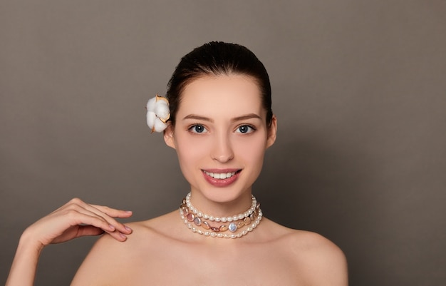 Retrato da beleza de uma mulher com uma flor no cabelo e um colar de pérolas em fundo marrom