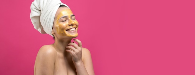 Retrato da beleza de uma mulher com uma toalha branca na cabeça e uma máscara nutritiva de ouro no rosto