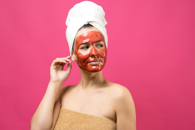 Retrato da beleza de uma mulher com uma toalha branca na cabeça e uma máscara nutritiva de ouro no rosto