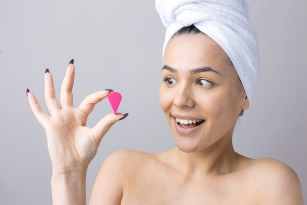 Retrato da beleza de uma mulher em uma toalha branca na cabeça com uma esponja para um corpo em vista de um coração rosa