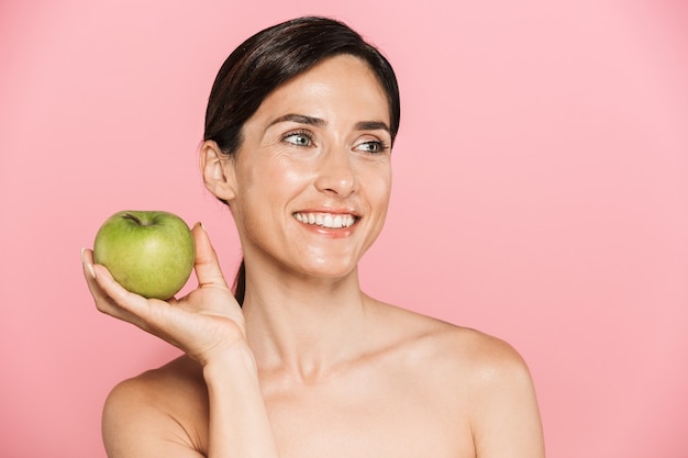 Retrato da beleza de uma mulher morena em topless sorridente atraente e saudável isolada, mostrando maçã verde