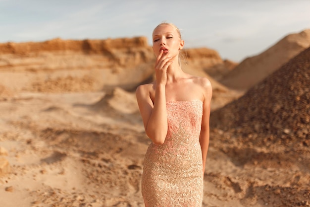 Retrato da beleza de uma mulher sensual vestida com um lindo vestido dourado, posando no deserto ao pôr do sol.