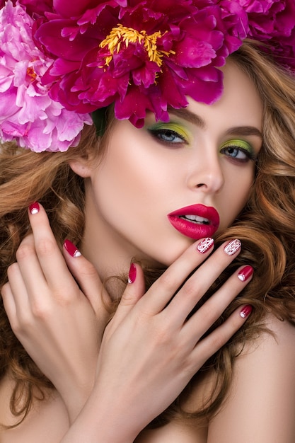 Retrato da beleza do close-up de uma jovem bonita com guirlanda de flores no cabelo, usando batom rosa brilhante e tocando seus lábios. Maquiagem de verão moderna e brilhante