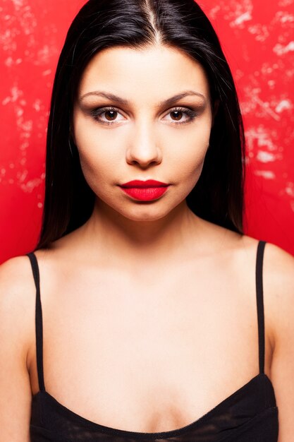 Foto retrato da beleza. retrato de uma jovem bonita olhando para a câmera em pé contra um fundo vermelho