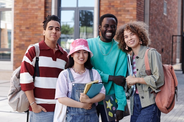 Retrato da cintura de um grupo diversificado de estudantes sorrindo para a câmera ao ar livre no campus da faculdade