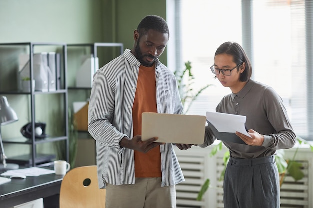 Retrato da cintura para cima de dois empresários étnicos afro-americanos e asiáticos discutindo projeto enquanto