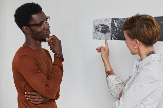 Retrato da cintura para cima de dois jovens discutindo arte enquanto exploram a exposição da galeria moderna,