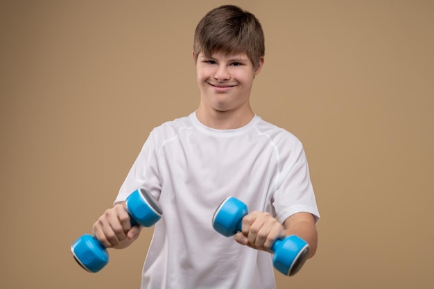 Retrato da cintura para cima de um adolescente satisfeito segurando um par de halteres nas mãos durante o treino