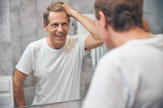 Retrato da cintura para cima de um homem de meia-idade satisfeito tocando seu cabelo com a mão