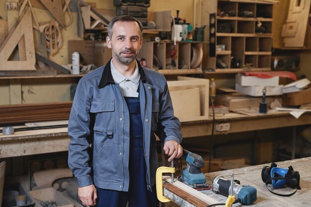 Retrato da cintura para cima de um trabalhador masculino sorridente olhando para a câmera enquanto está em uma oficina de fábrica copia s