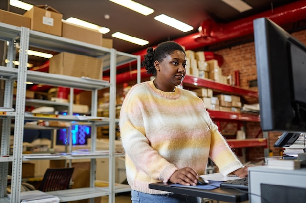 Retrato da cintura para cima de uma mulher negra adulta usando computador enquanto instala máquinas de impressão na industri