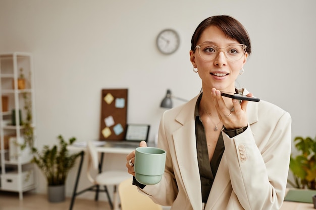 Retrato da cintura para cima do empresário feminino segurando smartphone e gravando mensagem de voz enquanto stan