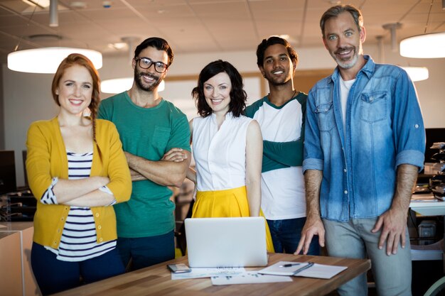 Retrato da equipe sorridente de negócios criativos em pé na mesa com o laptop no escritório