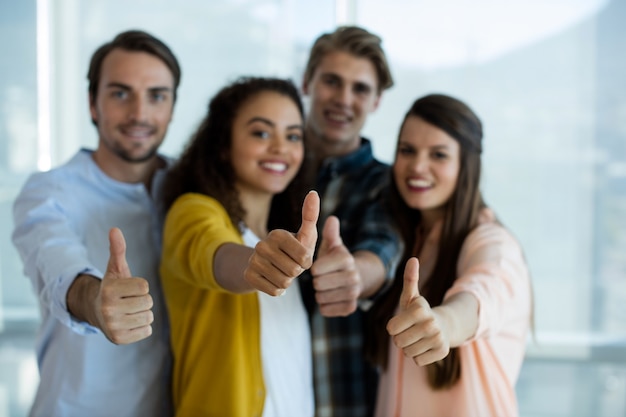 Retrato da equipe sorridente de negócios criativos mostrando os polegares para cima no escritório