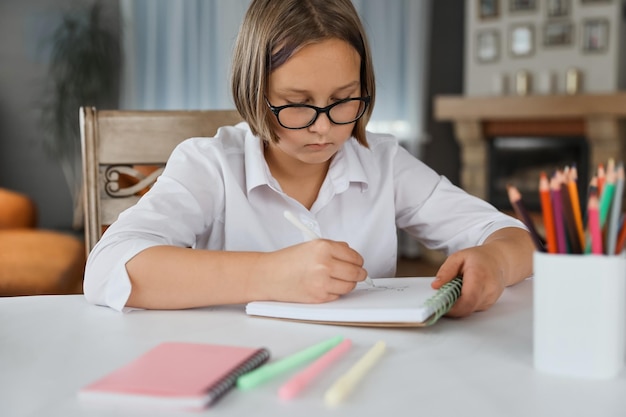 Retrato da estudante sentada à mesa dentro de casa e fazendo sua lição de casa A garota faz lição de casa em casa Aprendizagem a distância Lições educação lição de casa