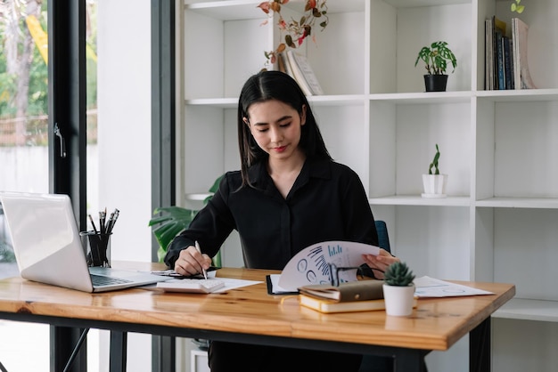 Foto retrato da jovem empresária asiática trabalhando no computador portátil fazendo finanças, análise contábil, relatório, dados e gráfico apontando no escritório.