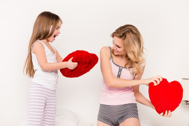 Retrato da mãe e da filha pequena travando uma batalha de travesseiros