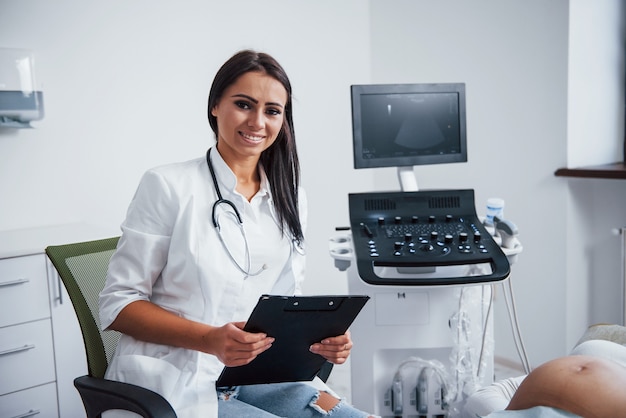 Foto retrato da médica obstétrica que se senta na sala da clínica com o dispositivo de ultra-som.