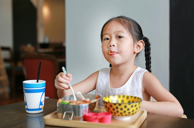 Retrato da menina asiática pequena da criança que come o café da manhã na manhã.