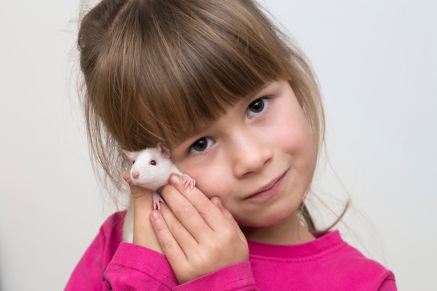 Retrato da menina bonito de sorriso feliz da criança com o hamster branco do rato do animal de estimação na luz. Manter animais de estimação em casa, cuidar e amar os animais.