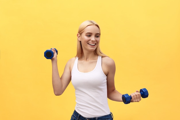 Retrato da menina consideravelmente desportiva que guarda pesos e sorriso. Isolado sobre o fundo amarelo.