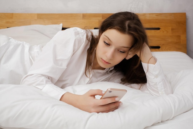 Retrato da menina deitada na cama com telefone celular