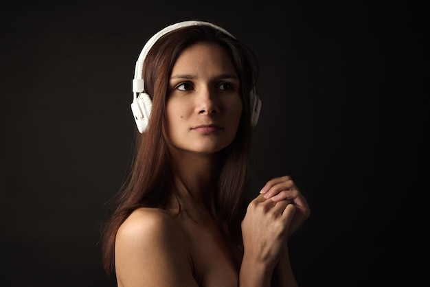 Foto retrato da moda beleza de linda morena menina morena isolada no fundo preto em fones de ouvido brancos com ombros nus. conceito de audiófilo, amantes da música e dispositivos de áudio sem fio