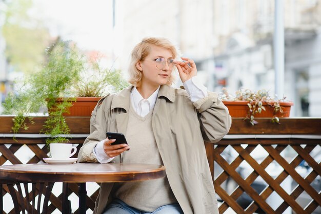 Retrato da moda da jovem localização à mesa com uma xícara de café, chá no café de rua.