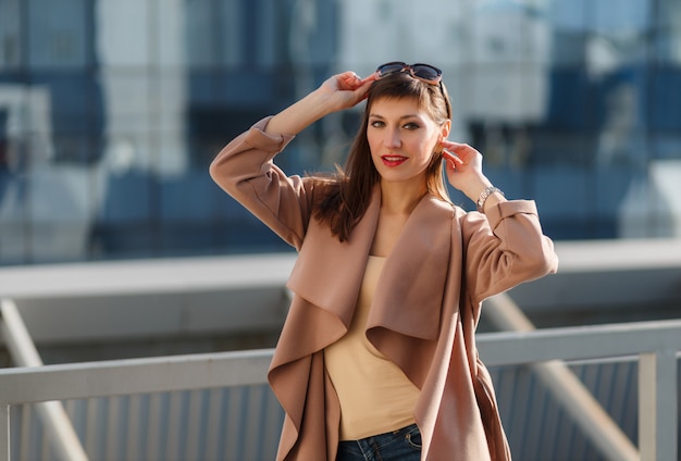 Retrato da moda da jovem modelo, com um belo casaco marrom bege, jeans e óculos de sol.