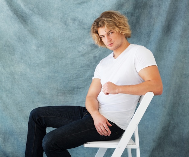 Retrato da moda de jovem em poses de camisa branca em estúdio sobre fundo azul